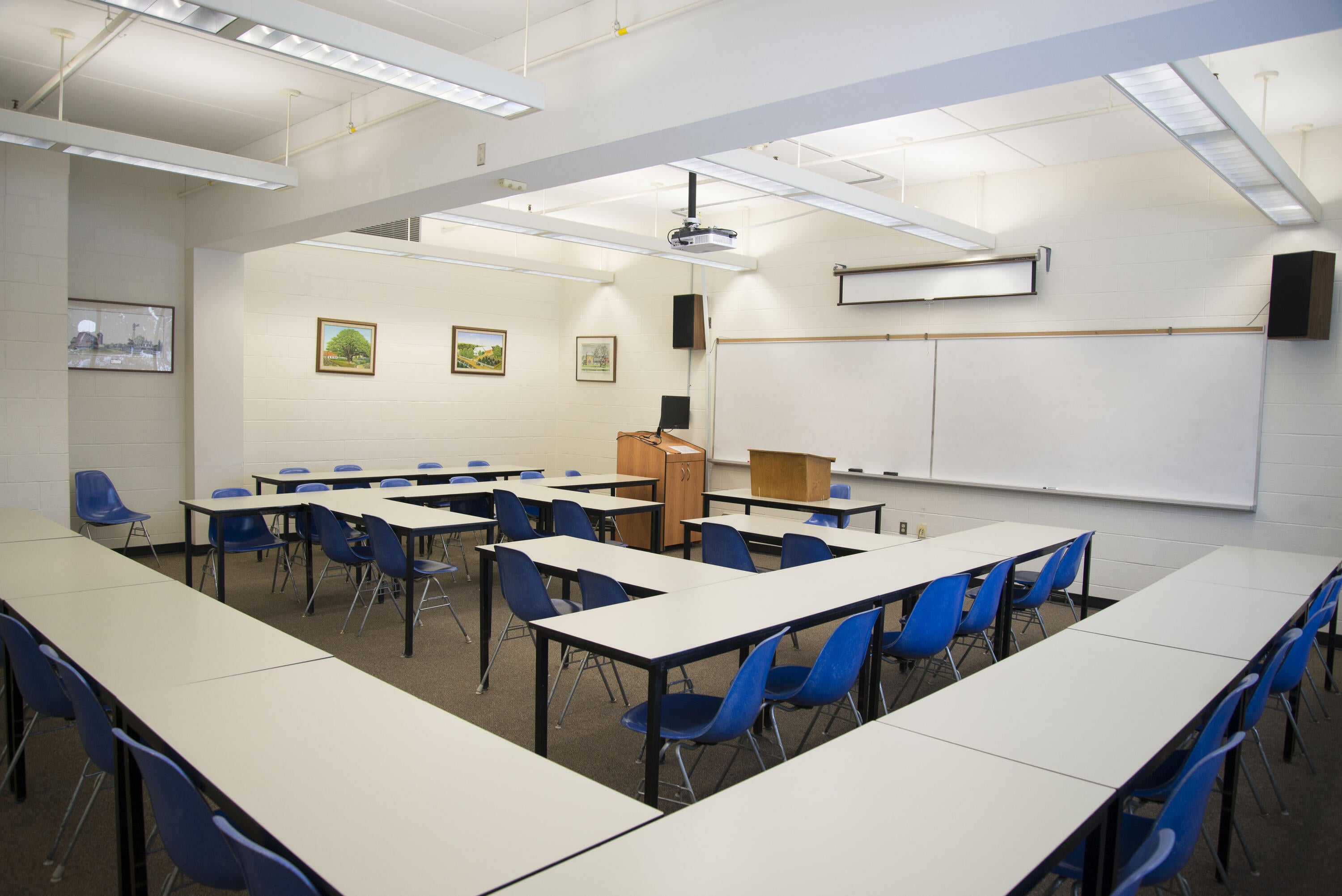 Classroom with long tables, chairs, a whiteboard, and a projector
