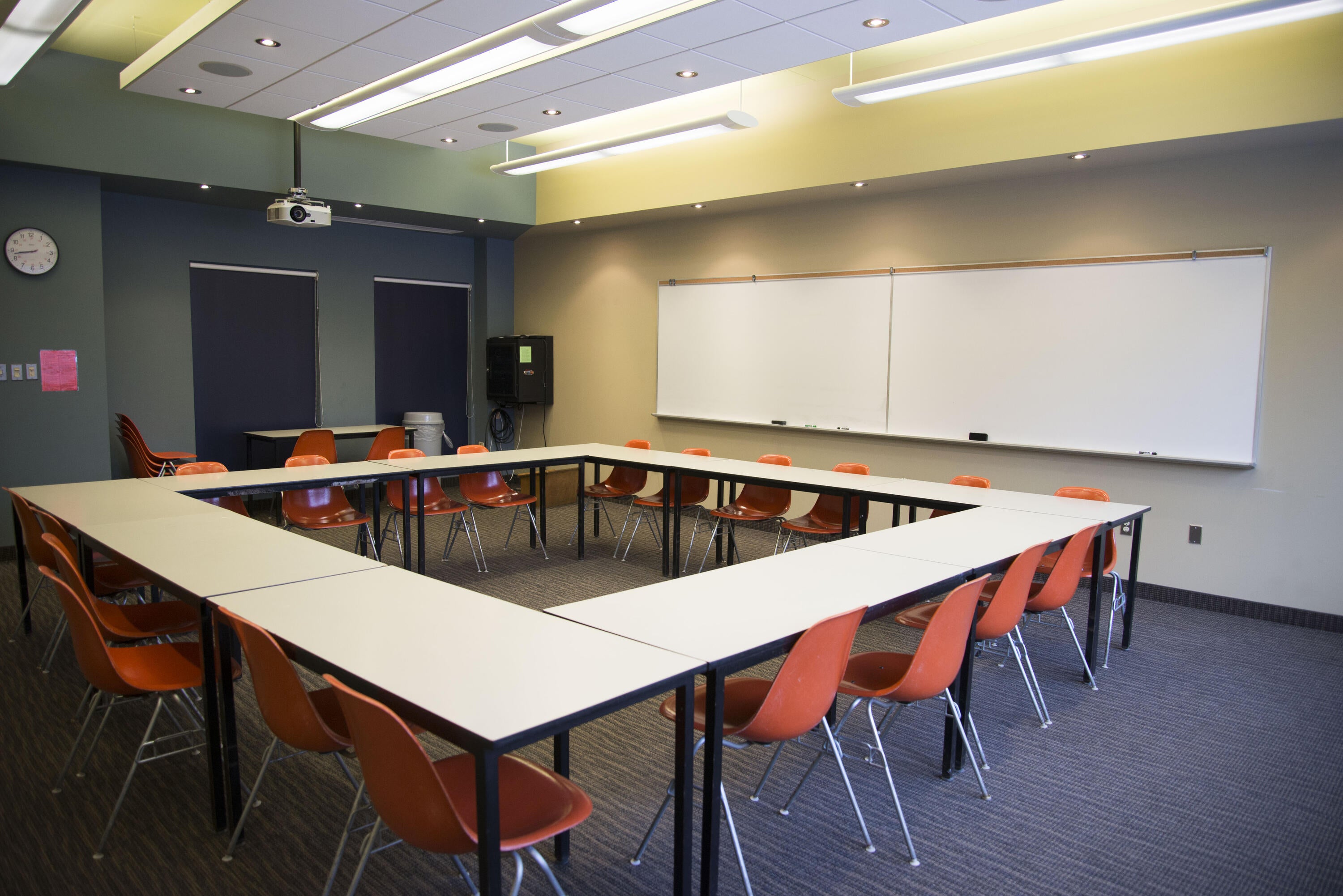 Classroom with a square of tables, chairs, a whiteboard, a projector, and an upright piano