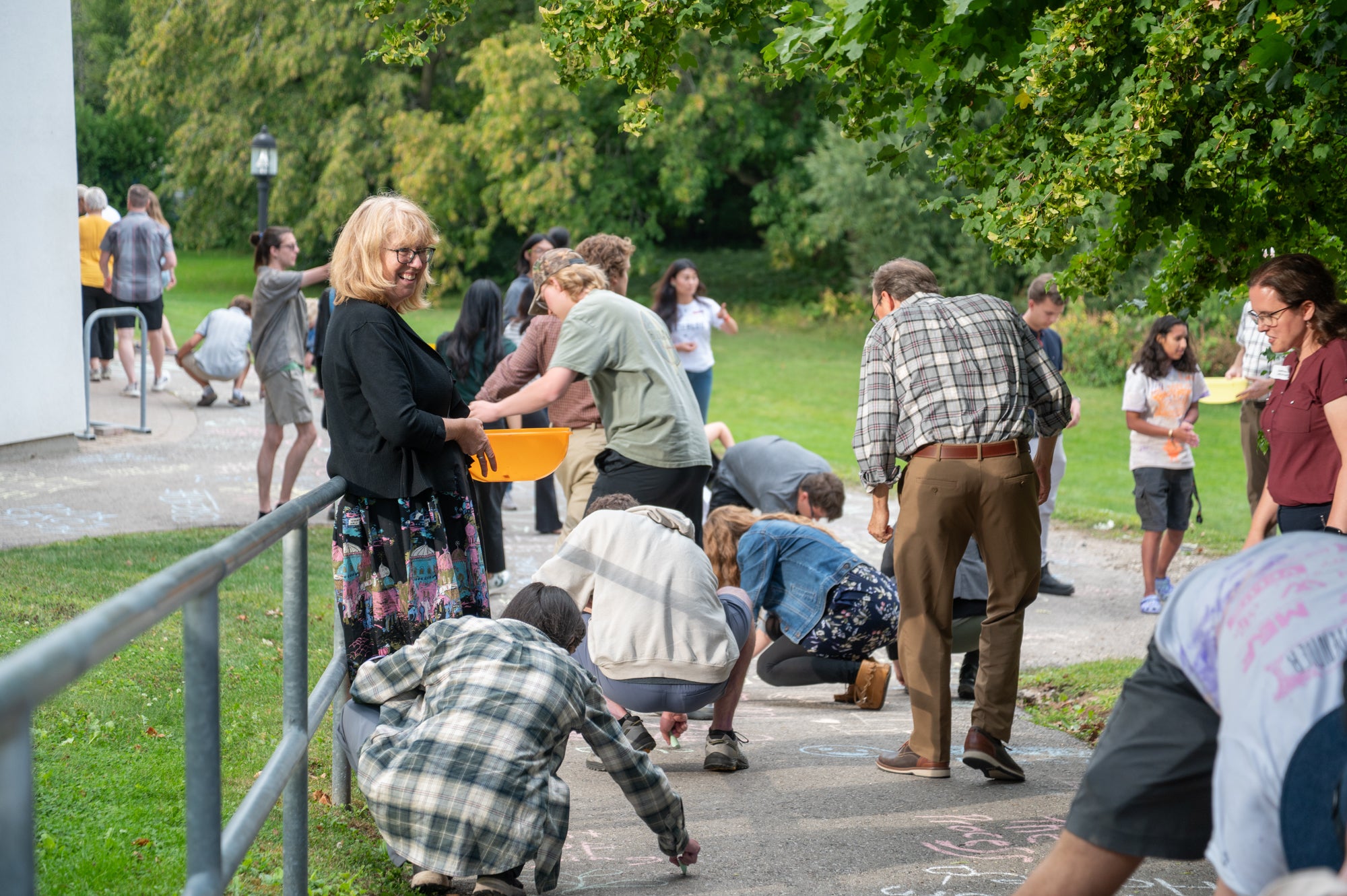 Carol Penner holds a bowl of chalk as people draw on the sidewalk