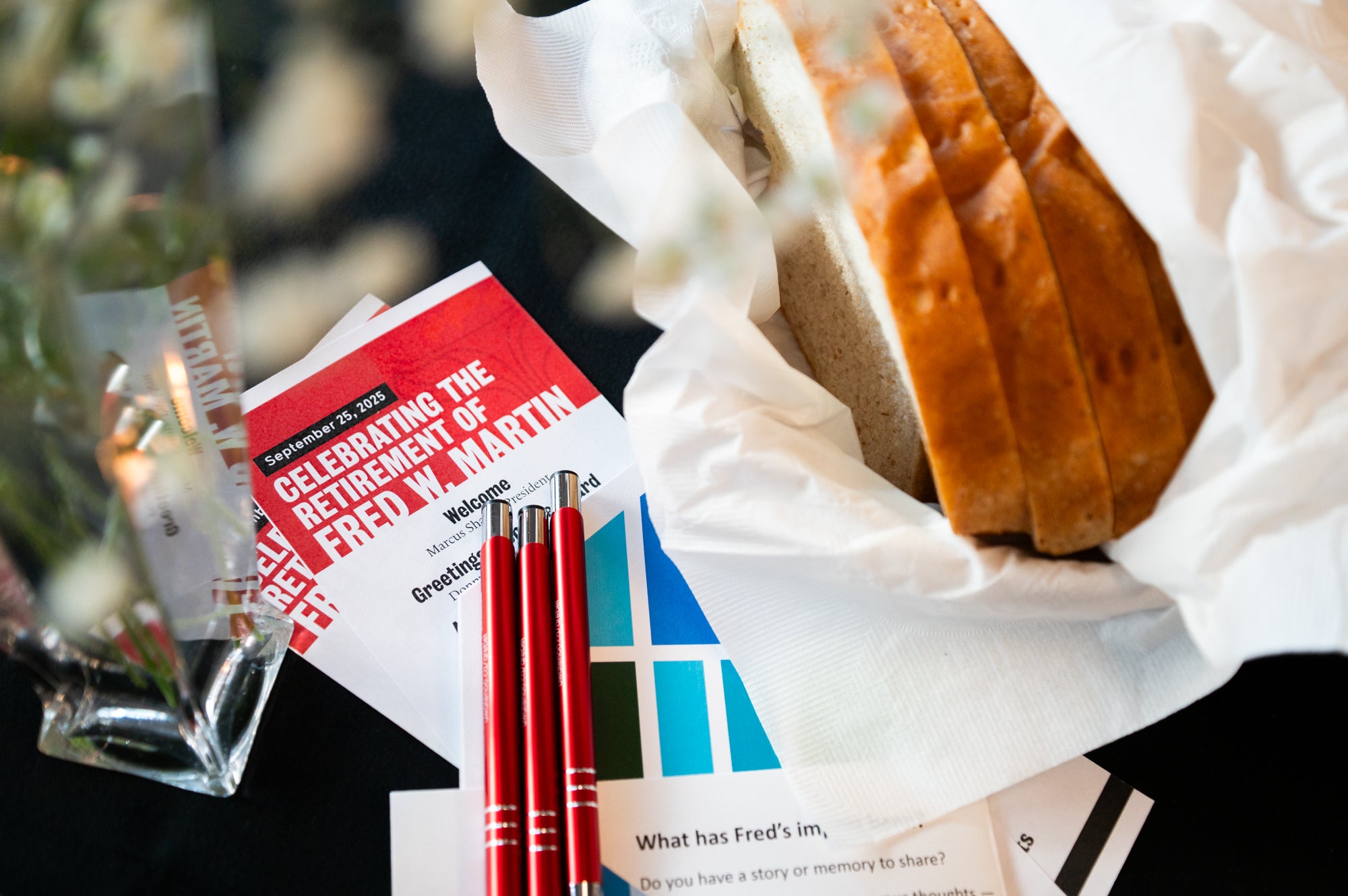 A close up of a table with a loaf of bread, pens, and paper program. 