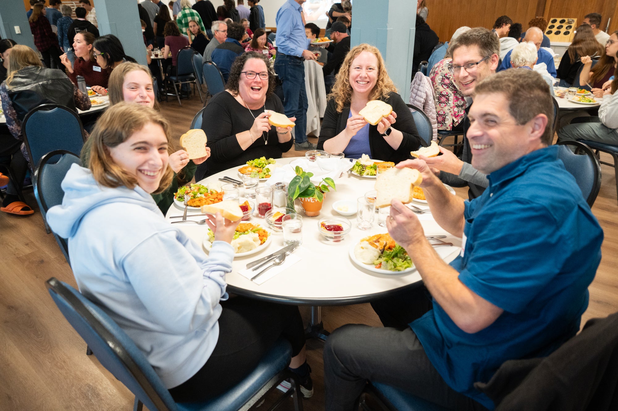A group of young adult Grebel alumni hold up pieces of bread together, smiling