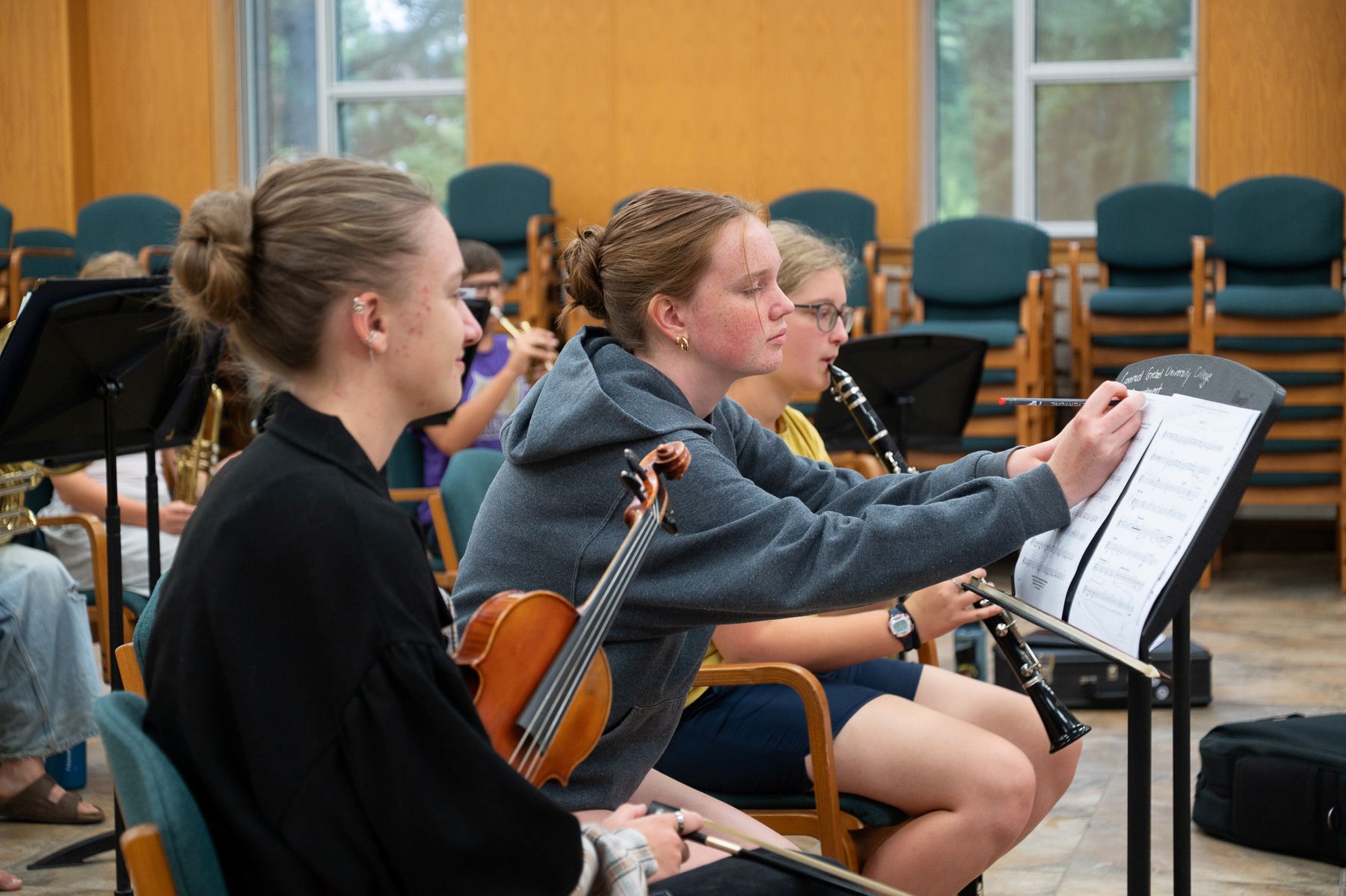 Three students with violins, one write on a piece of music