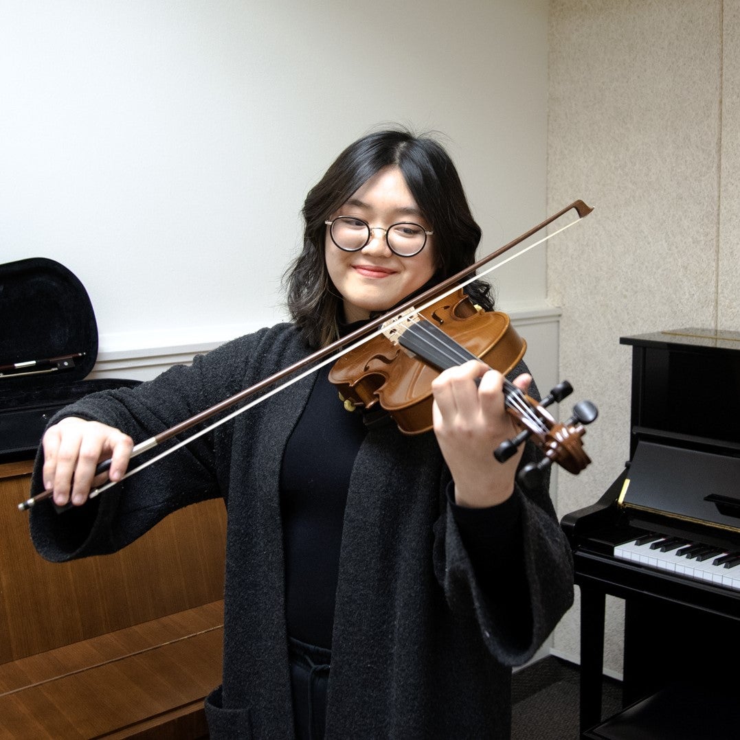 Darley Dau playing violin in a piano practice room.