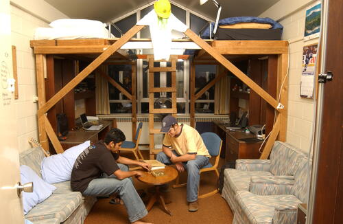 Two students from 2003 play cards in their residence room, with a bunkbed structure in the background