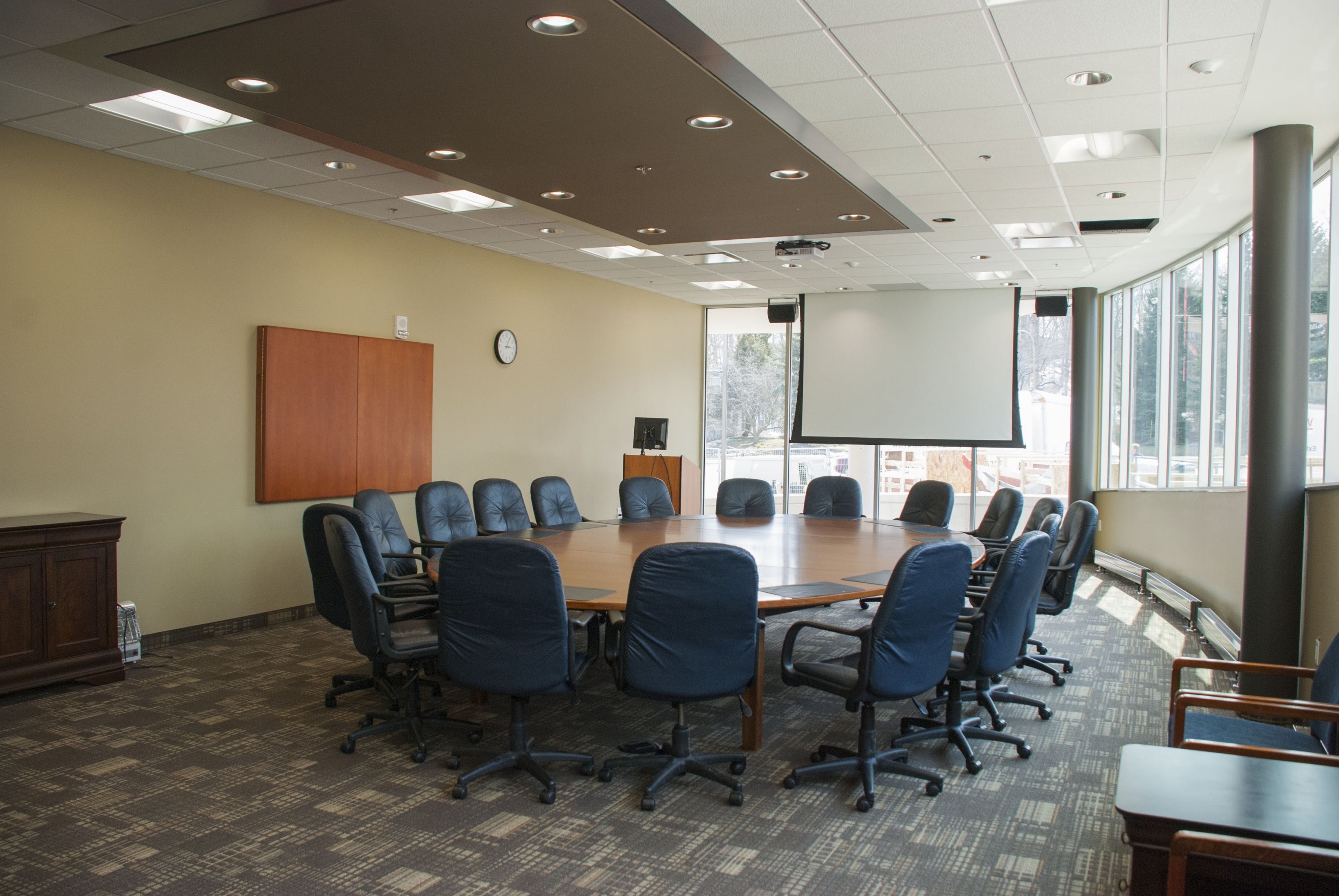 Large board room with wooden table, board chairs, a projector, and large windows