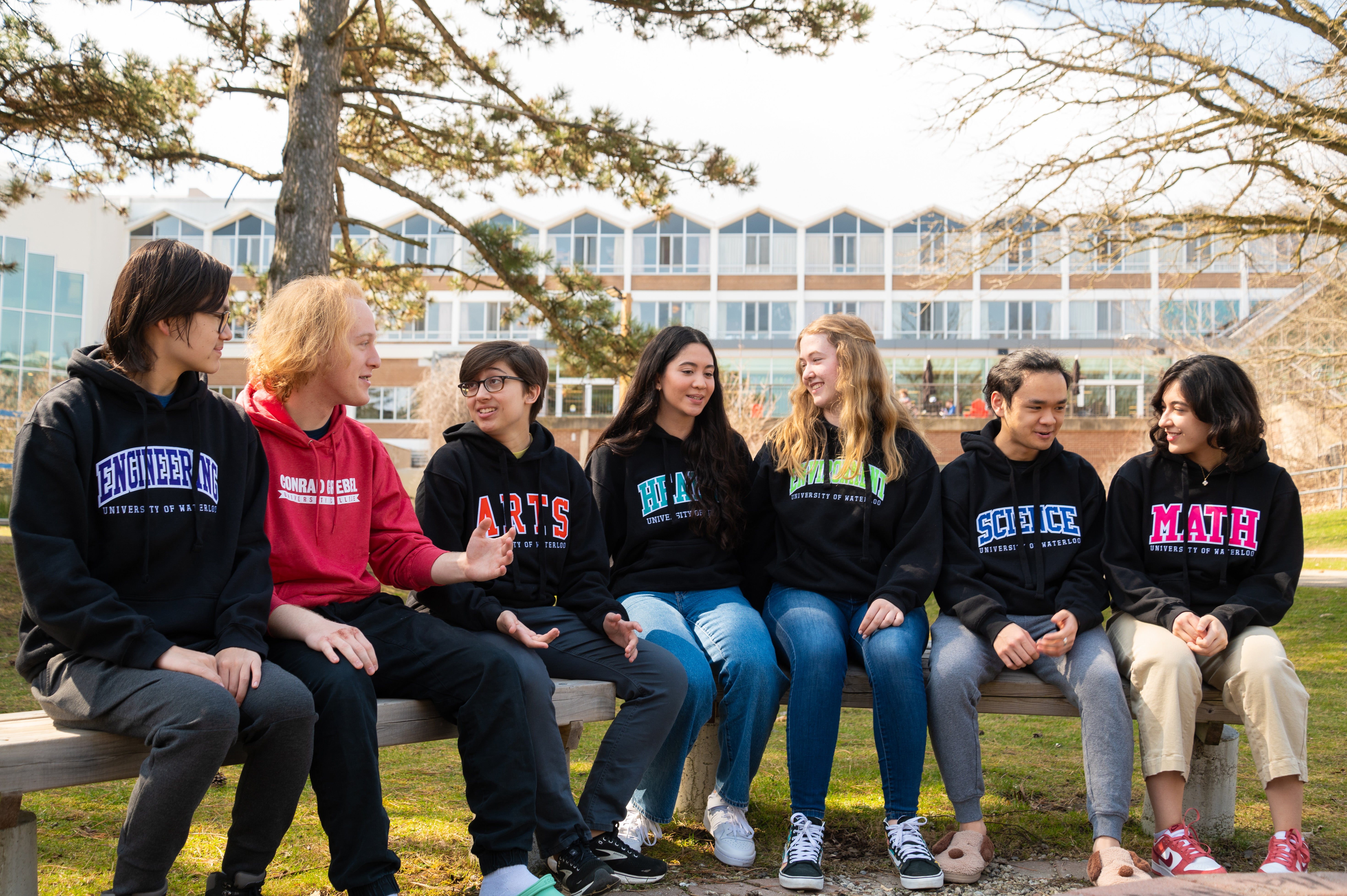 A group of Grebel students wear their faculty sweaters, sitting outside Grebel