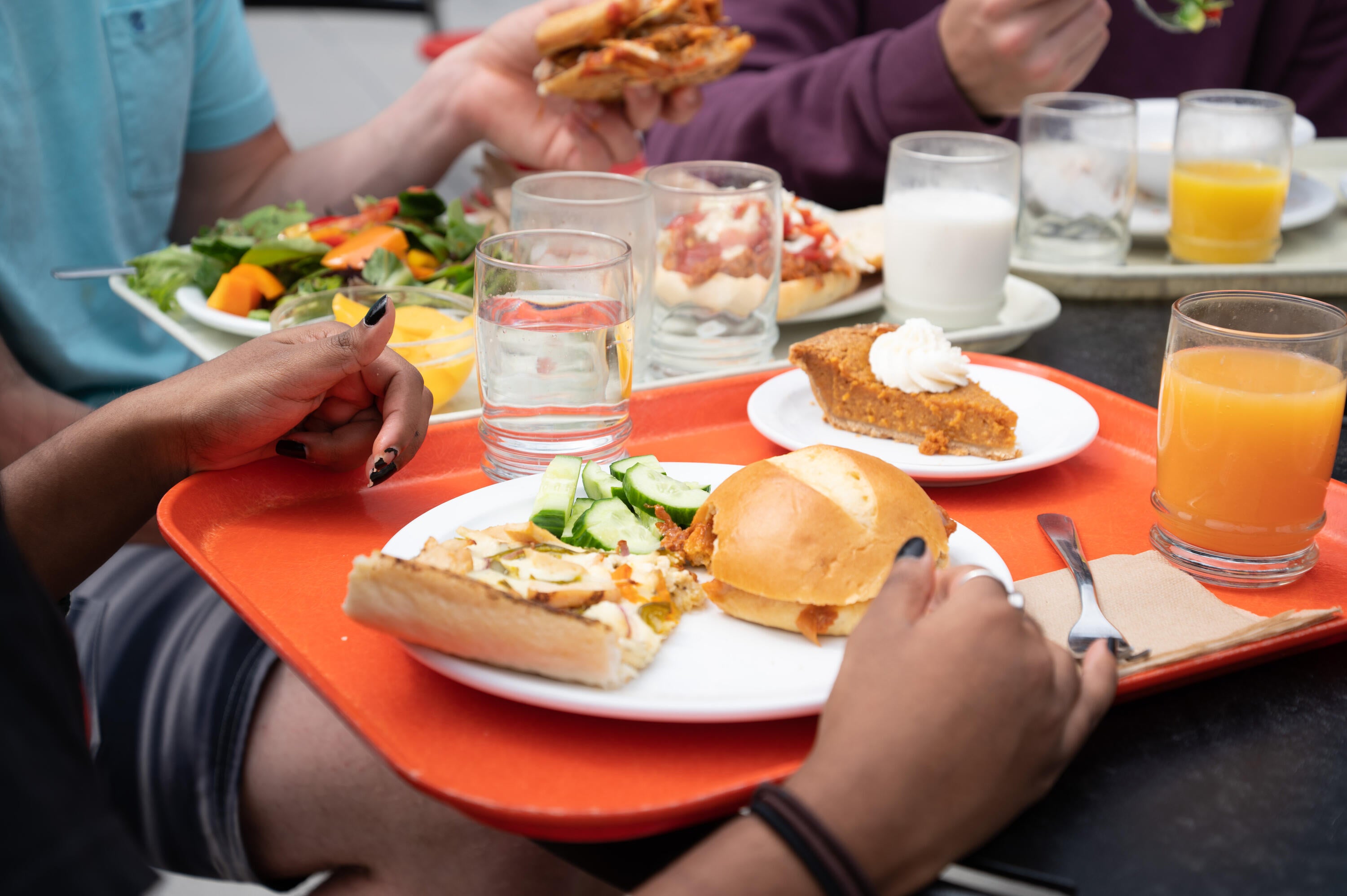 two trays with various food items and glasses of juice and water