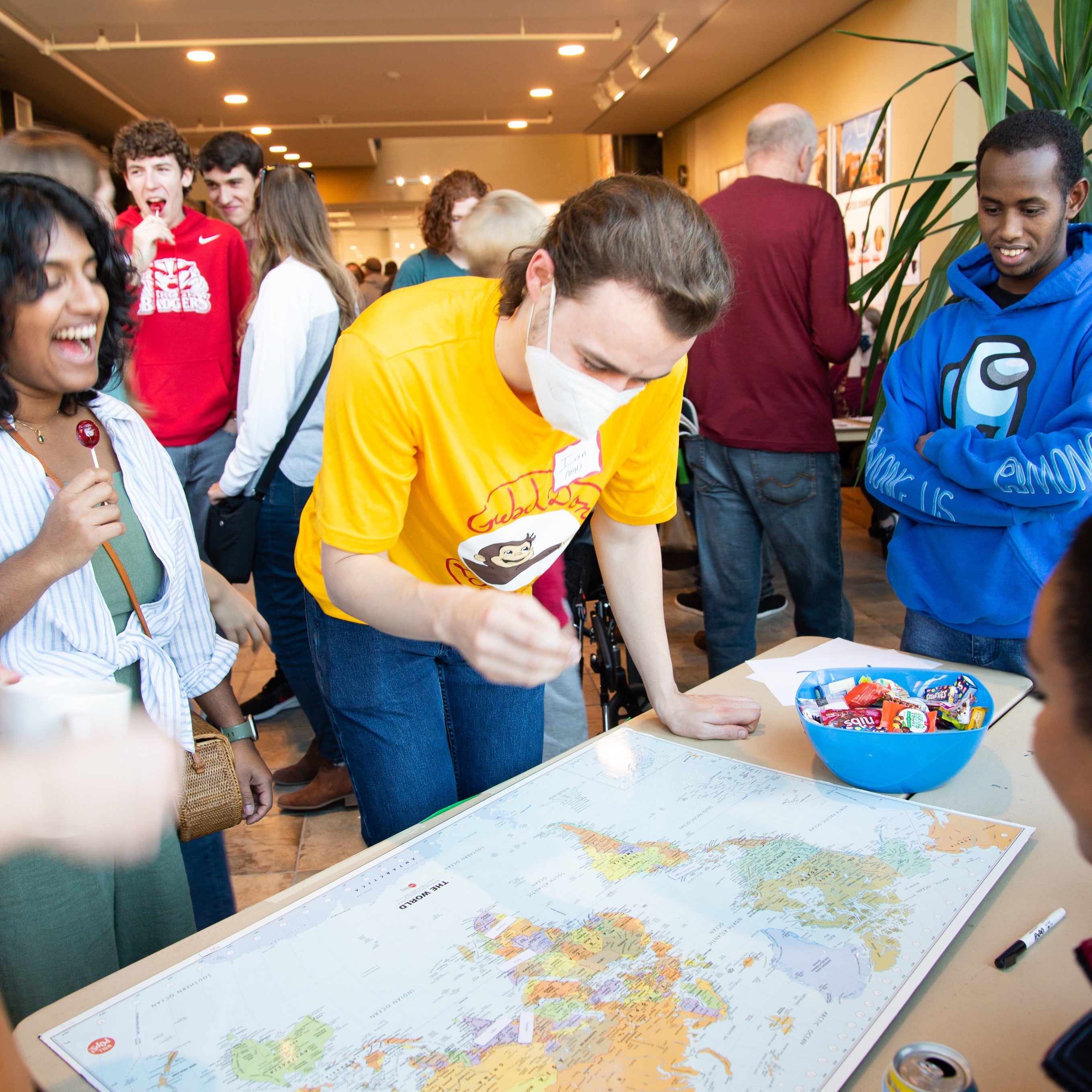 Grebel students in bright single colored shirts looking at a world map 