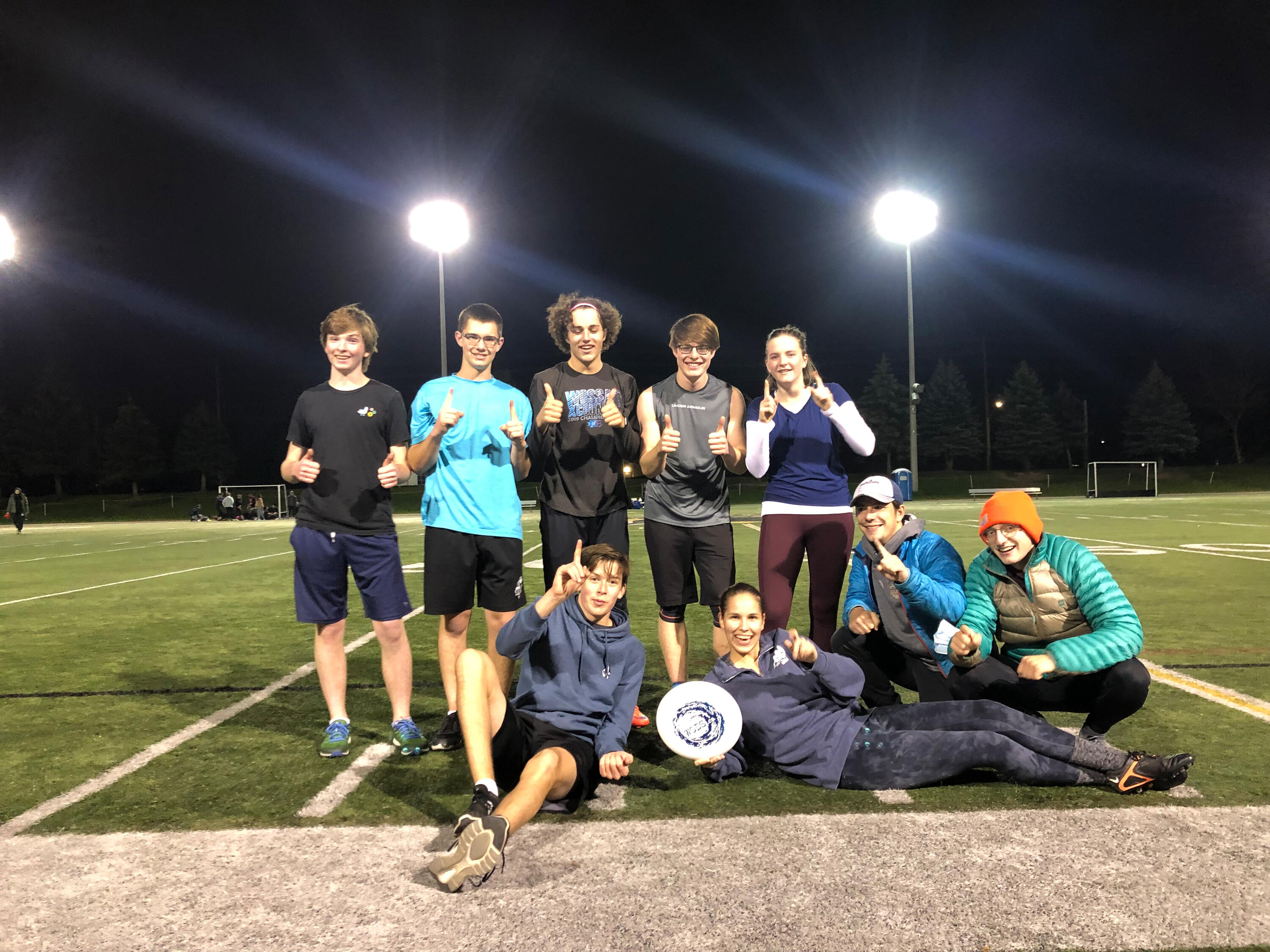 students posing with a Frisbee on a football field 