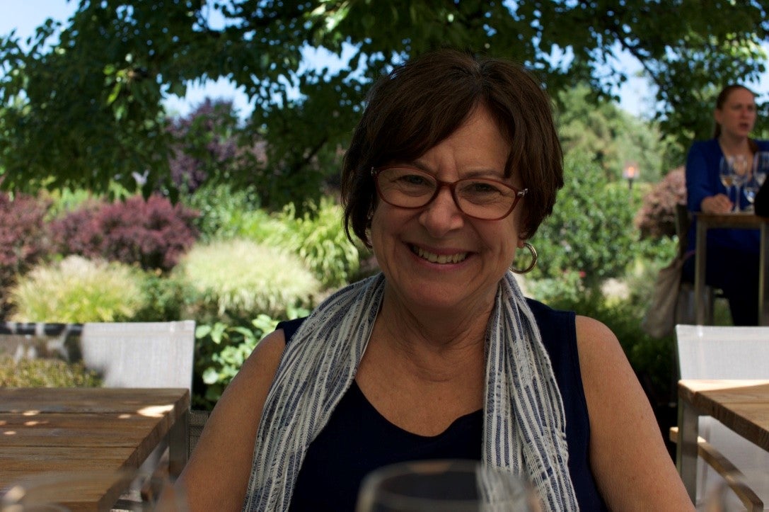 Janet Ramsey smailes, holding a coffee cup in front of a shaded garden