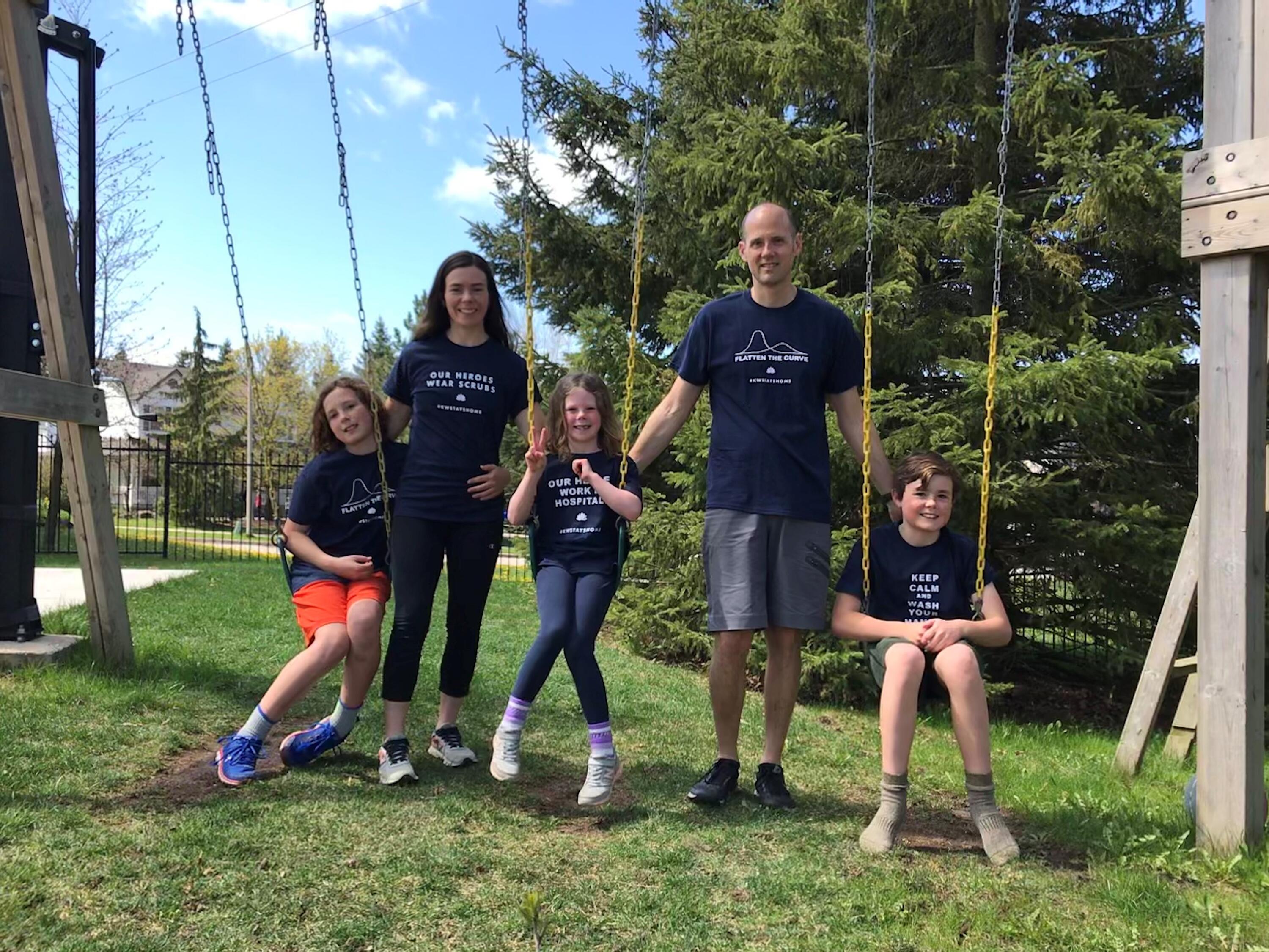 Jay Green stands at a swing set with his wife and two kids. They wear black shirts that promote flattening the COVID-19 curve.