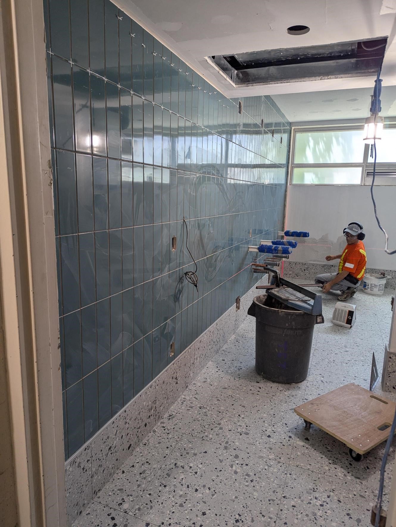 Tile on bathroom wall completed up to ceiling, man continuing work