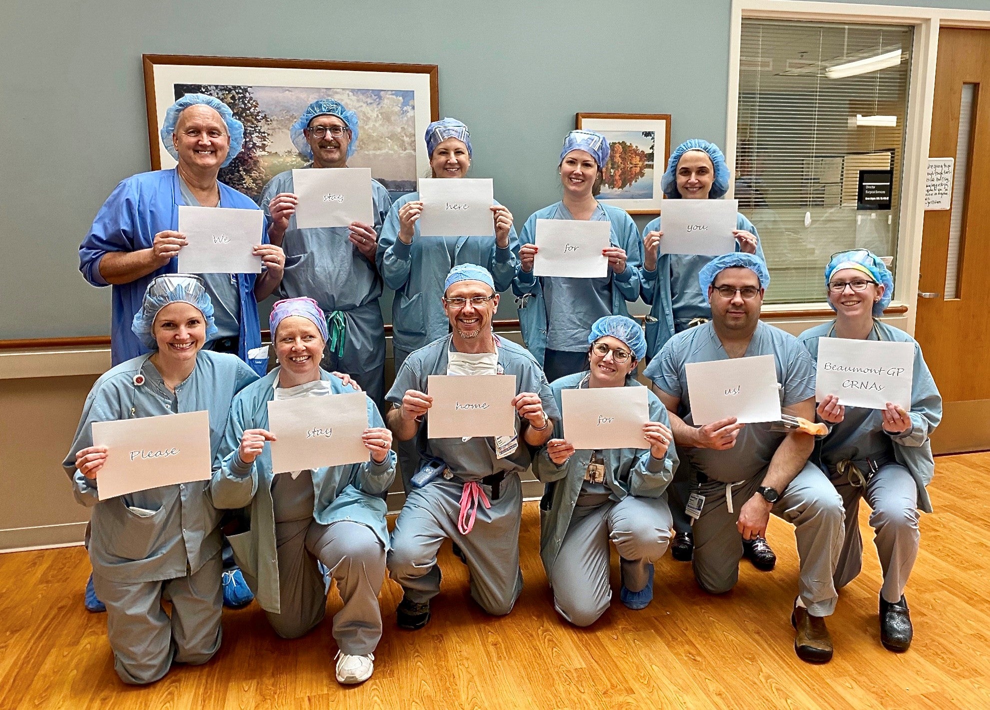 Mike stands in a group picture with the health team, each dressed in scrubs holding up paper that says 