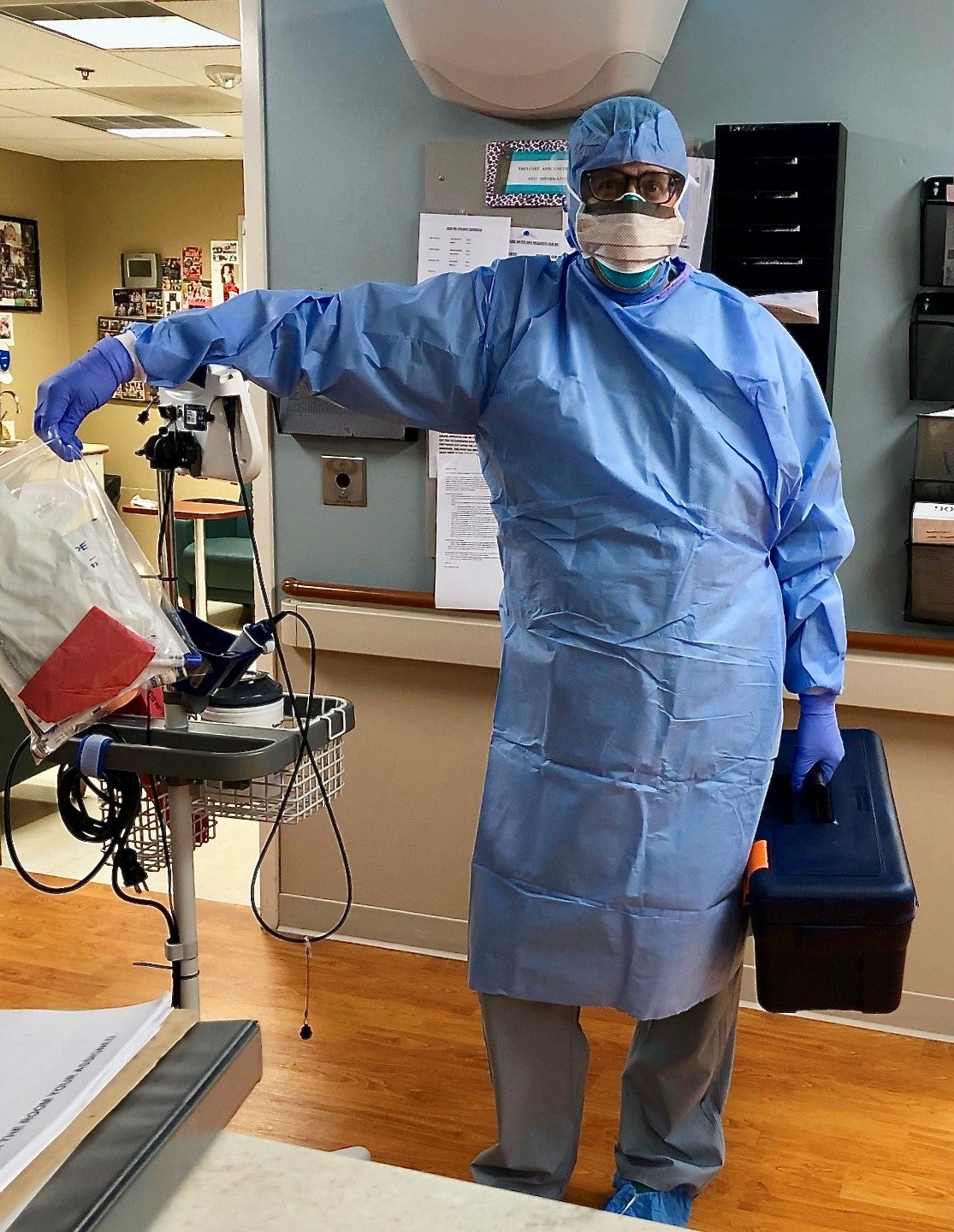 Mike stands with a videoscope station and holds a toolbox while dressed in protective equipment. He is about to assess a patient with suspected COVID-19
