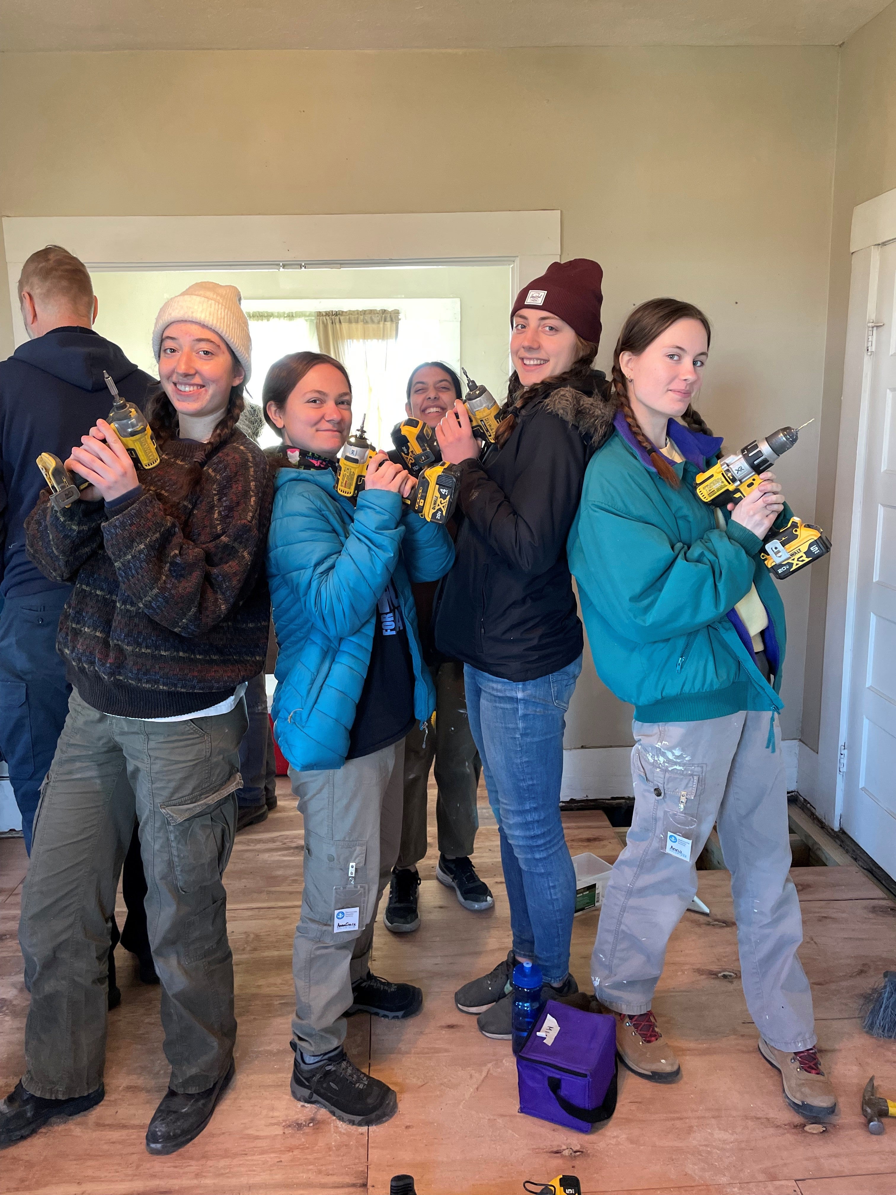 five students posing with drills while repairing a home 