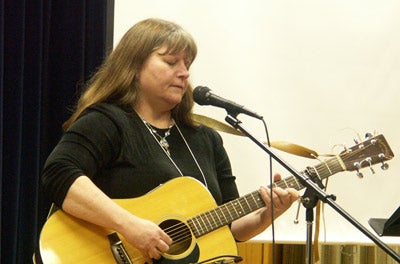 A woman performs a song on the guitar for the crowd.