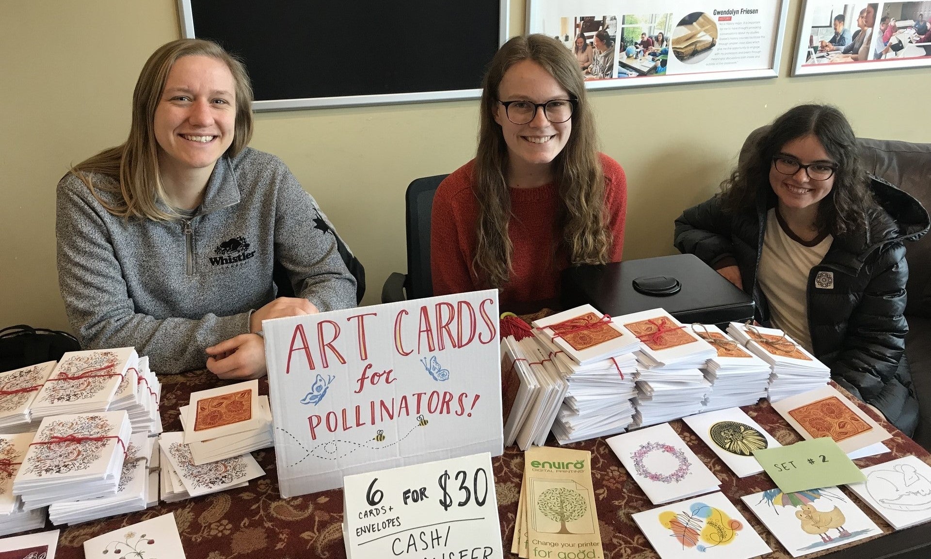 three students sitting at a table covered in cards for pollinator garden 