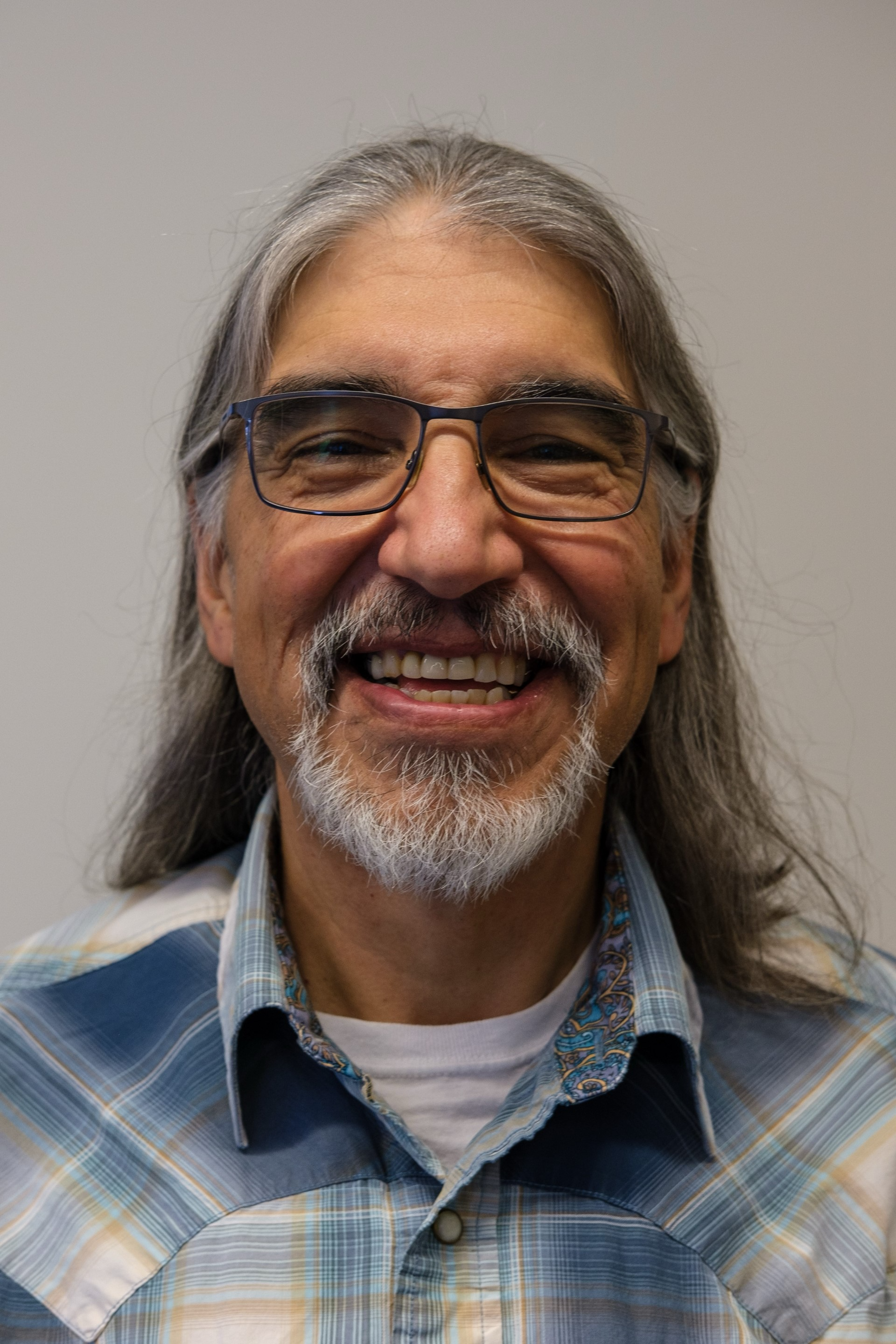 Ray Aldred, with silver hair and a short beard smiles for a photo.