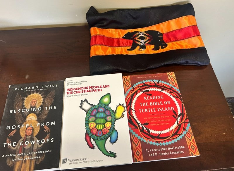 Three indigenous teachings books and a cloth with orange, red, and a black bear.