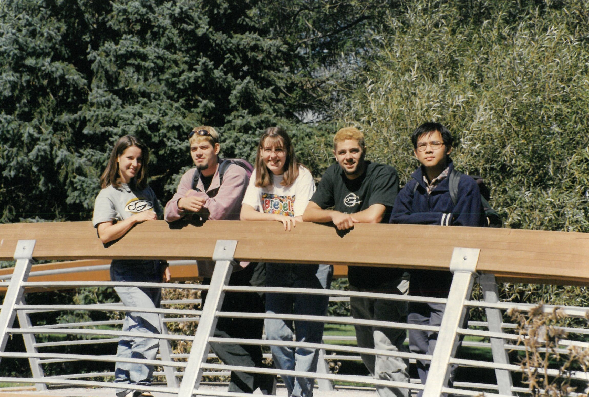 Five students standing on a bridge outside and smiling