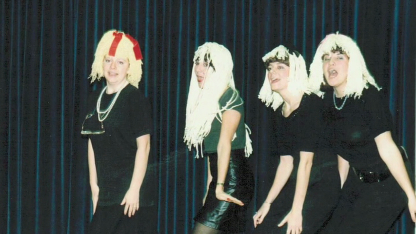 four students in white wigs and black dresses perform a skit during a talent show in the 80s