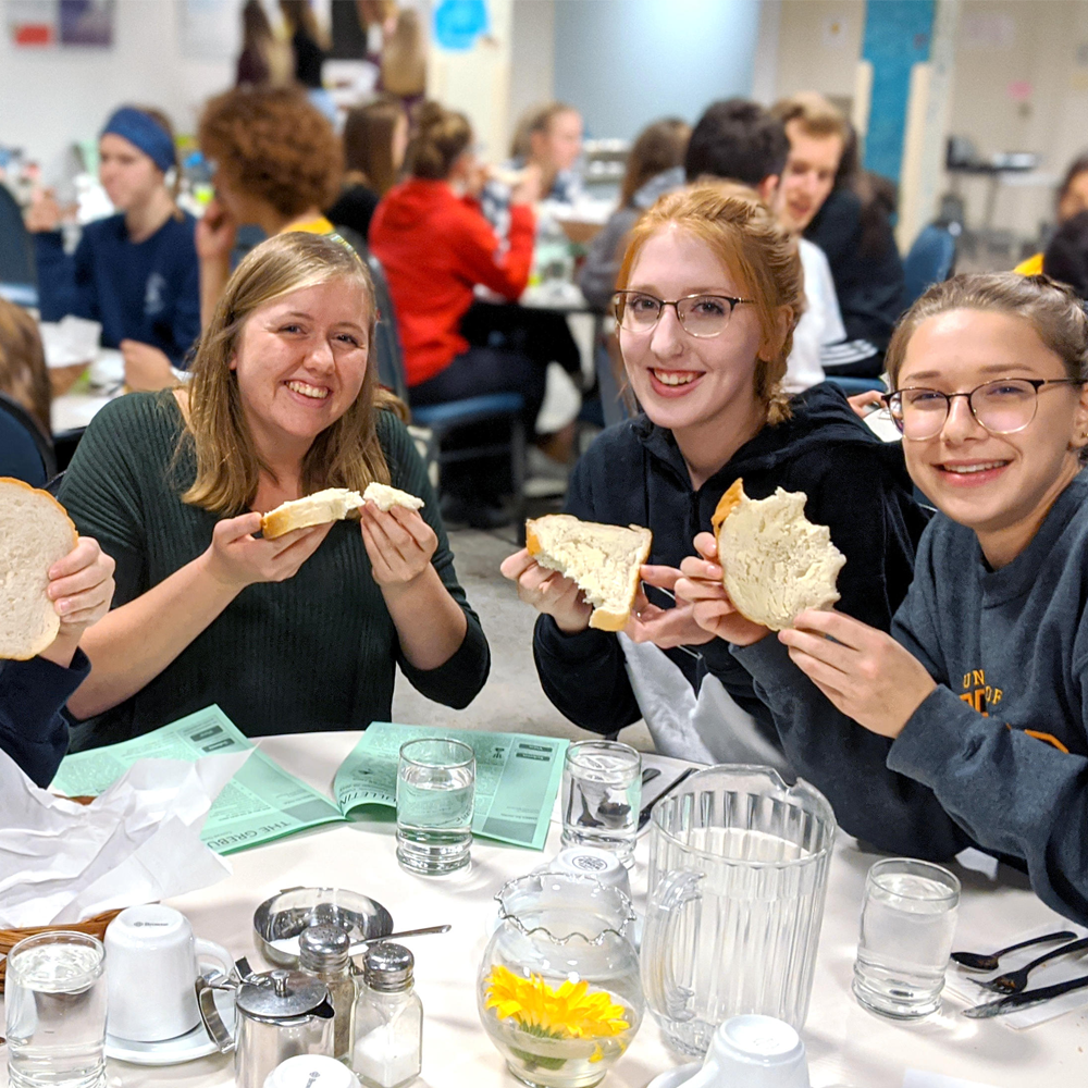 Three students at a table hold up pieces of bread