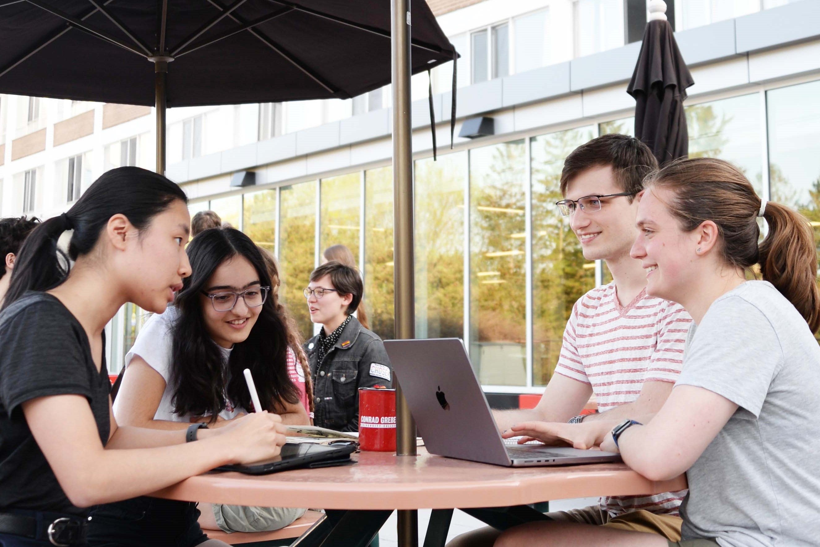 Students talking over open books and laptops at a table on the Grebel patio