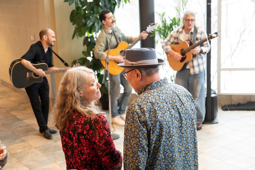 Dr. Tom Lee talking to someone in front of 3 people playing guitars 