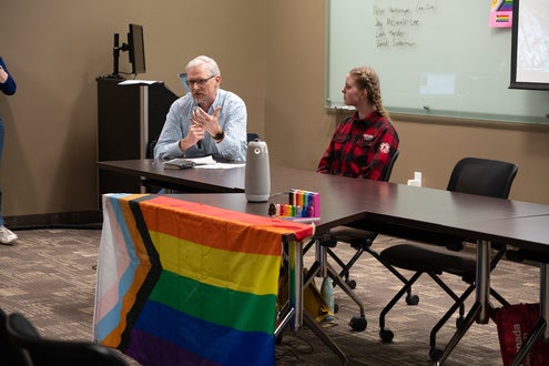 Jay and Professor Derek Suderman sitting at desk with a pride flag on display