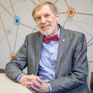 Edmund Pries posing at desk hands clasped 