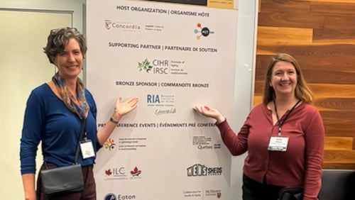 Jane Kuepfer and Kate Dupuis stand in front of a banner