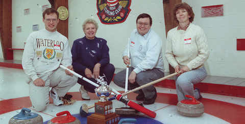Curlers kneeling at button with trophy and brooms.