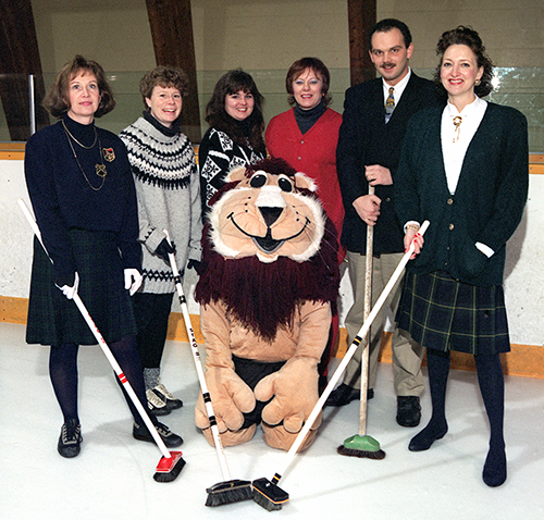Curlers with brooms and stuffed lion.