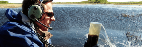 Prof. Roland Hall is wearing helicopter head-phones while collecting sediment from a lake.
