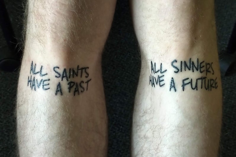 Tattoo under knees, reads "all saints have a past" and "all sinners have a future".