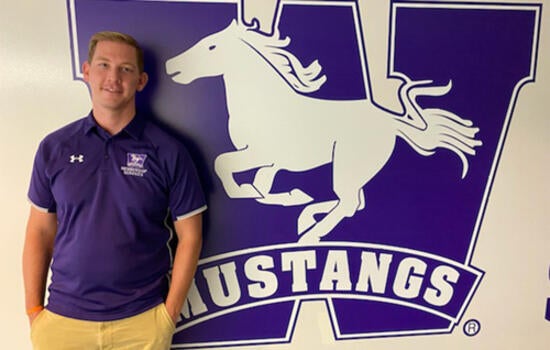 Chad standing in front of Western Mustangs wall crest.