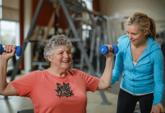 Older adult lifting arm weights with personal trainer