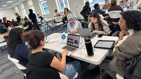 Groups of students collaborate at seminar table while facilitators check in.