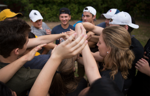 Students outside join hands in team effort.