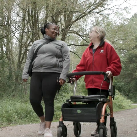 Two women walking on a nature trail, with one using a walker.