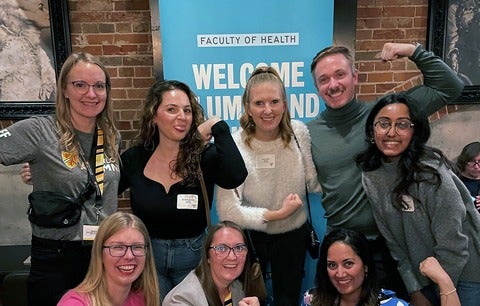 Group of smiling and laughing alumni wearing nametags at an event.