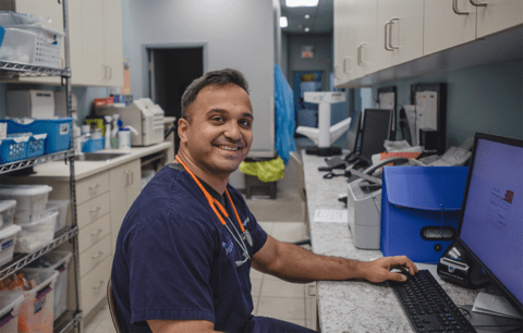 Dr. Ammar Bookwala smiles wearing stethoscope in medical clinic.