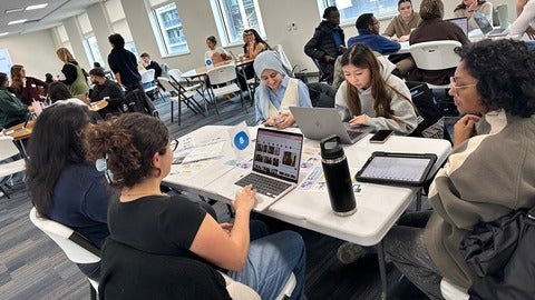 Groups of students collaborate at seminar table while facilitators check in.