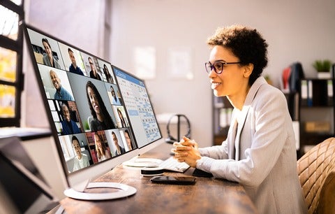 Women sitting at a desk and monitor talking to group of people online.