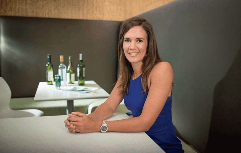 Erin Hobin sits at table with bottles of alcohol in the background.