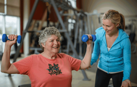 Kylie Sullivan guides woman in gym through weightlifting exercise.