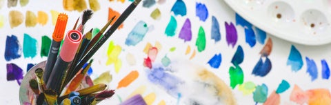 Jar of paint brushes on brightly painted paper.