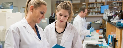 Professor and student wearing lab coats review a file in a lab.