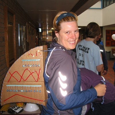 A female wearing a backpack made by a box and decorated with strings and shinny buttons