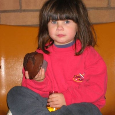 A girl sitting down on a chair holding a brownie and a bottle of juice 